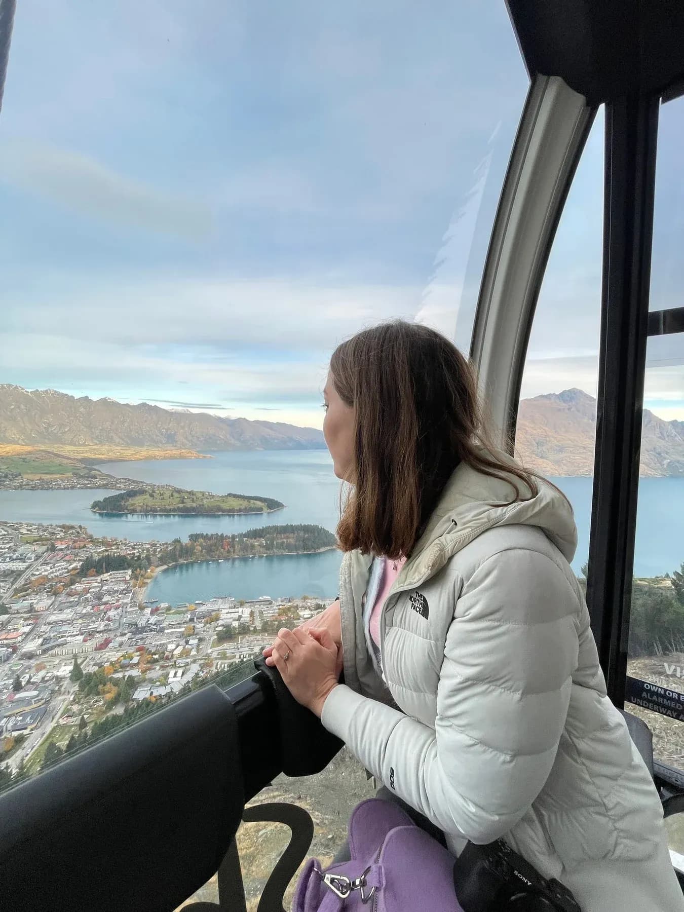 A passenger looks across Queenstown and Lake Wakatipu from a gondola cabin.